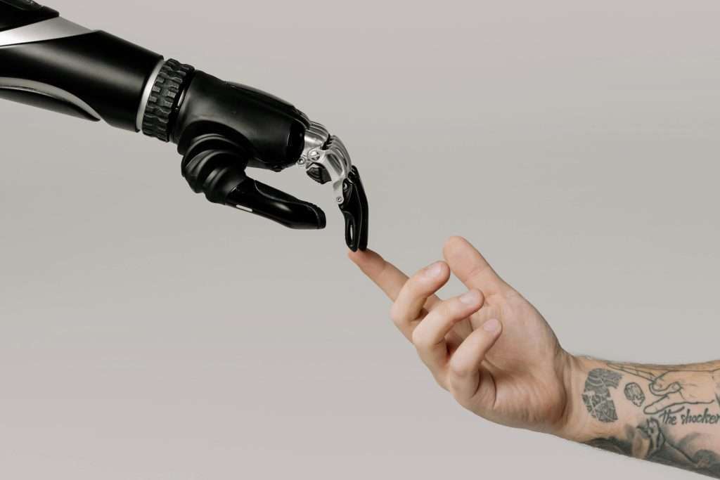 Navigating AI in the Writing Industry—Part 1: Friend or Foe? 2 A robotic hand, guided by AI, touches fingertips with a tattooed human being.